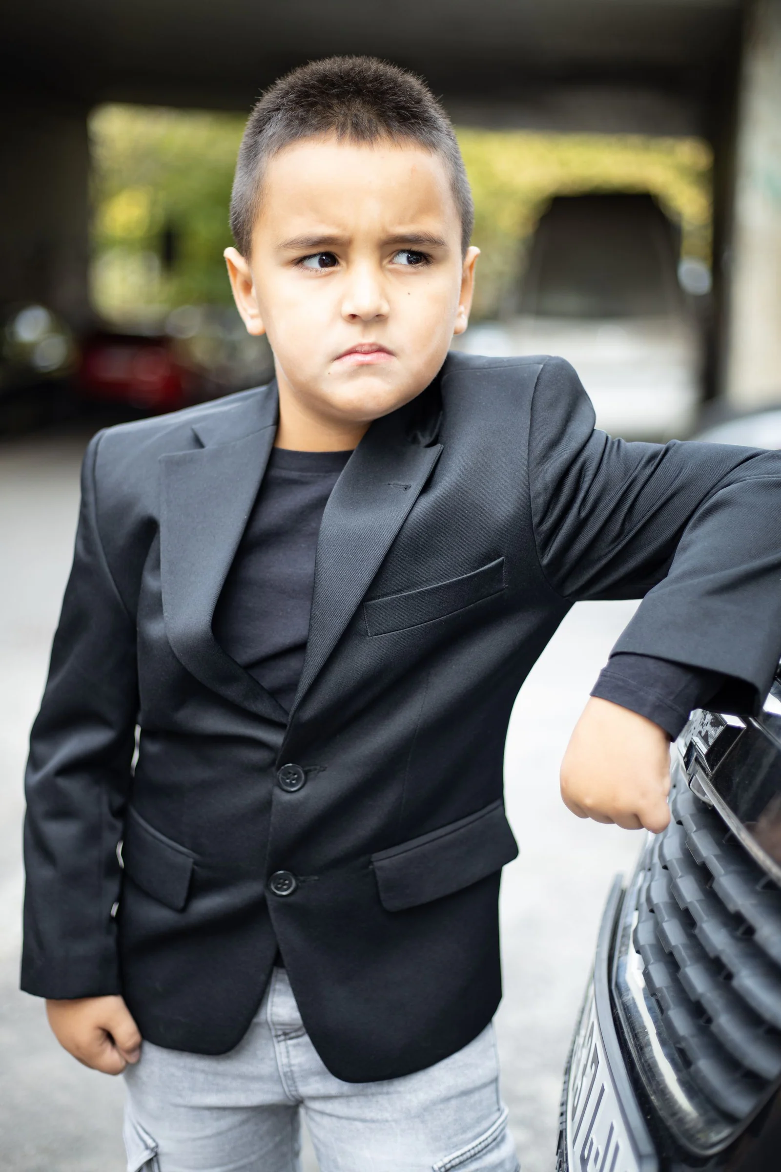 Confident boy in suit leaning on car