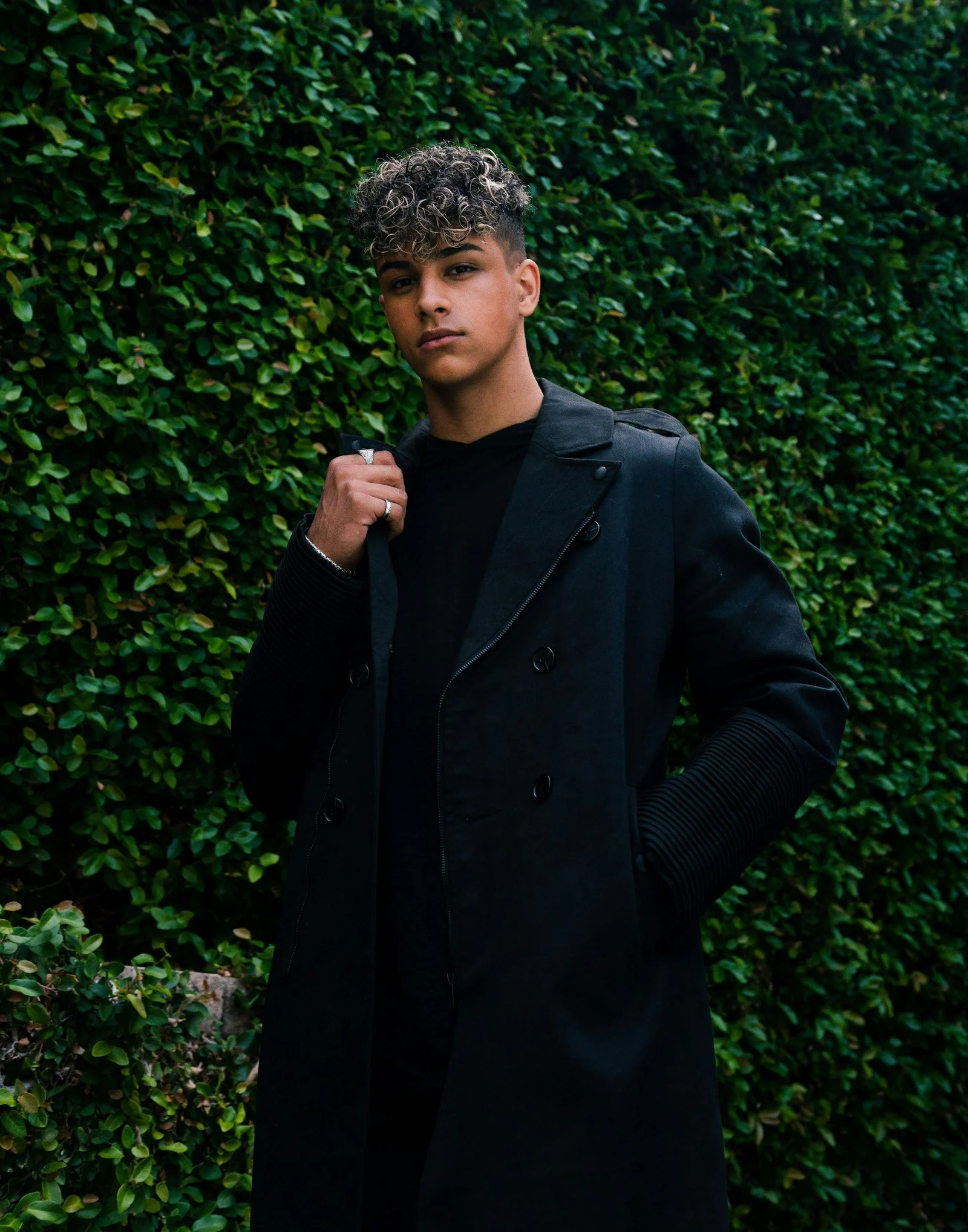 Man in black coat standing near green plant