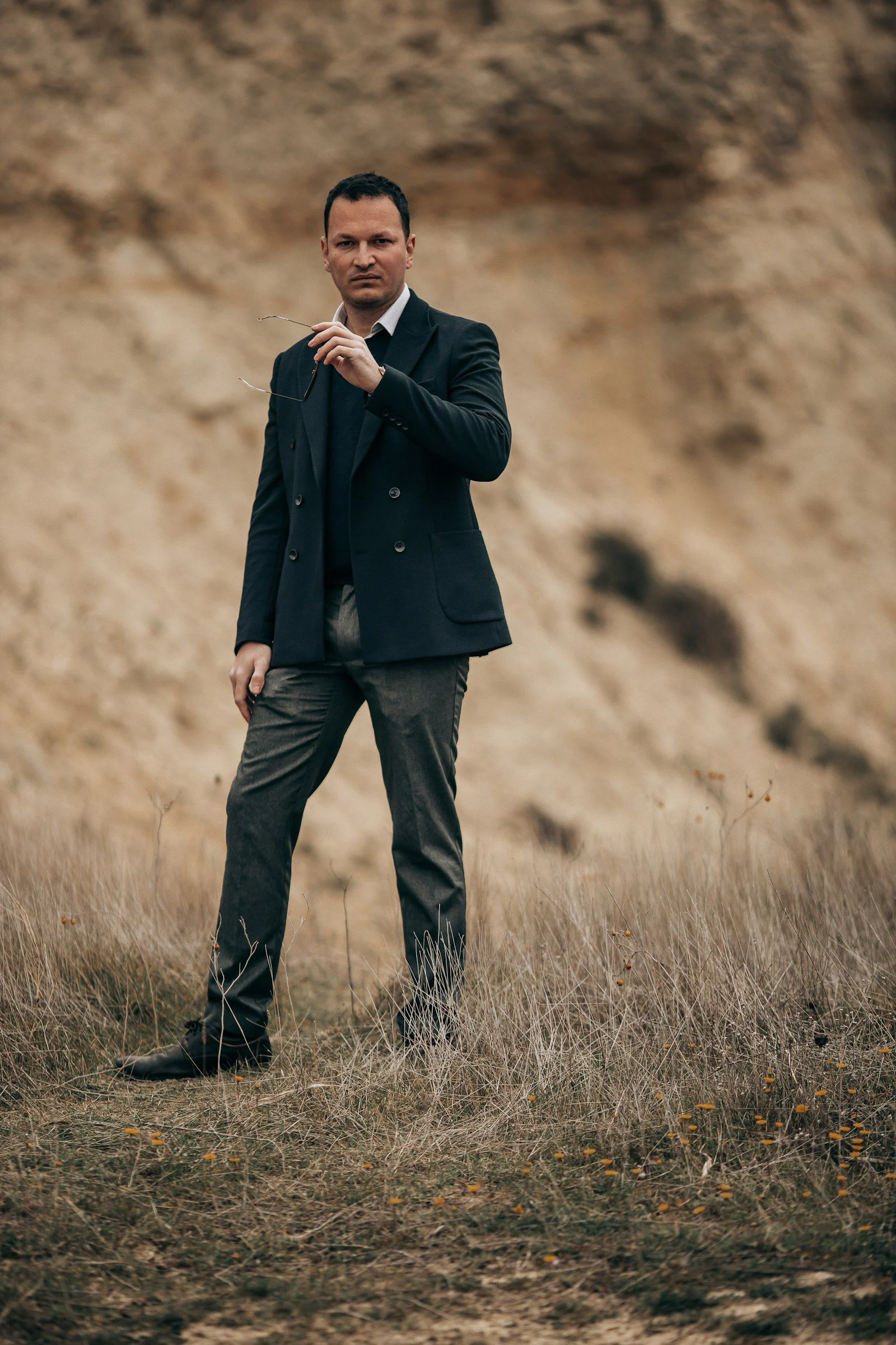 Man in suit holding glasses in a dry landscape