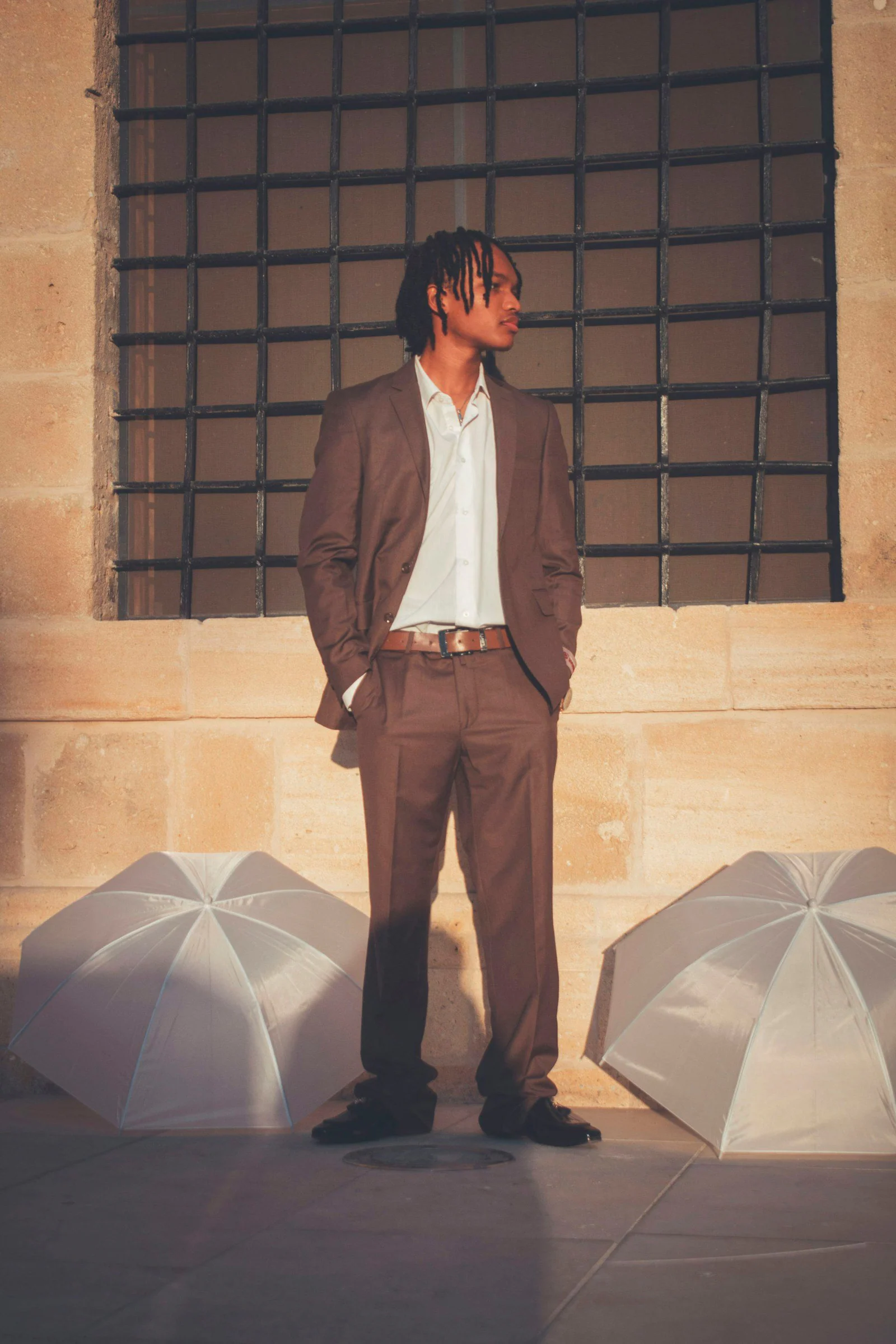 Man in a brown suit standing outdoors with umbrellas