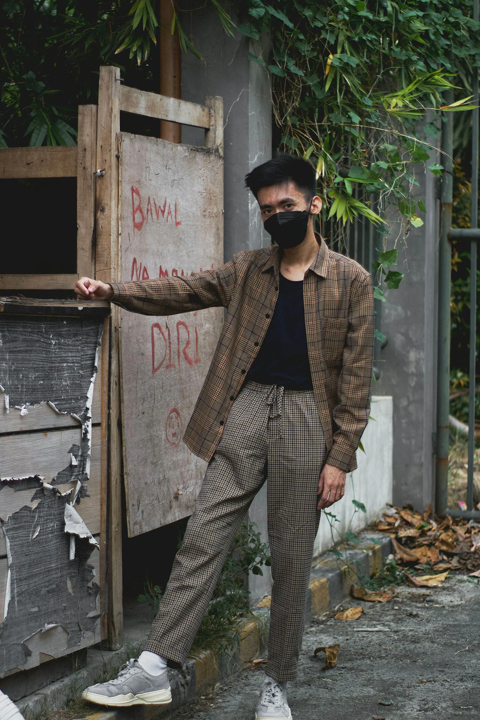 A man wearing a face mask leaning against a wall