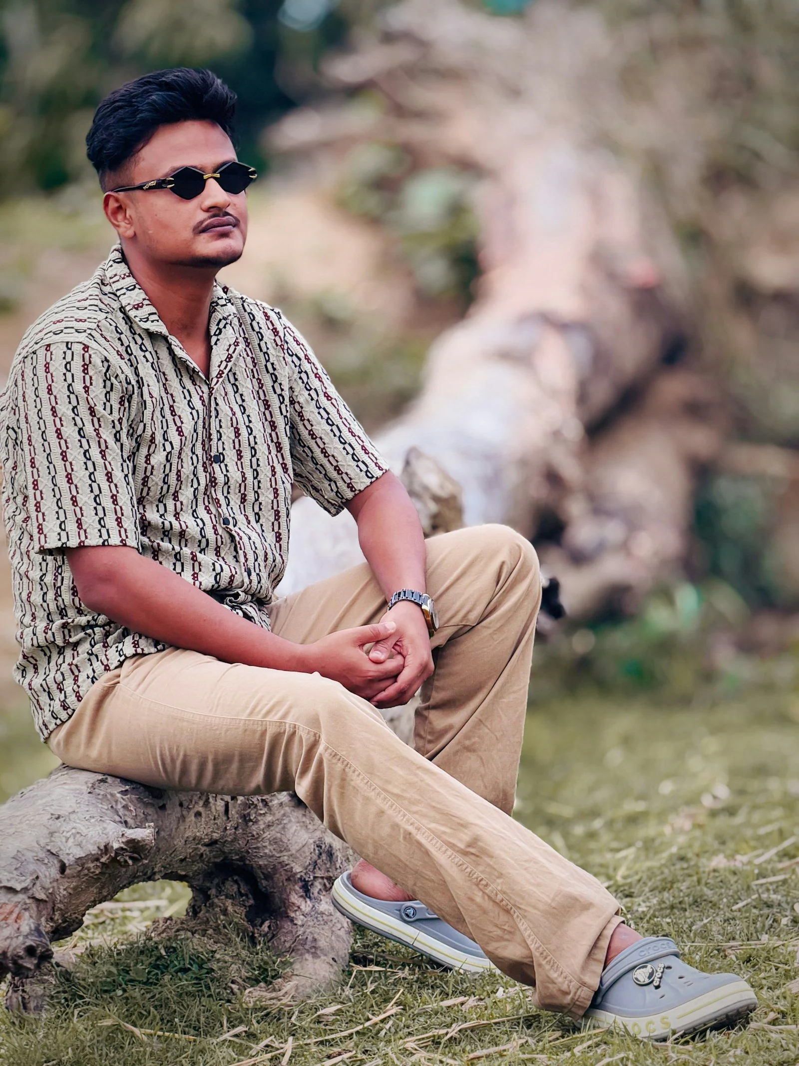 Stylish man in sunglasses sits on a log outdoors