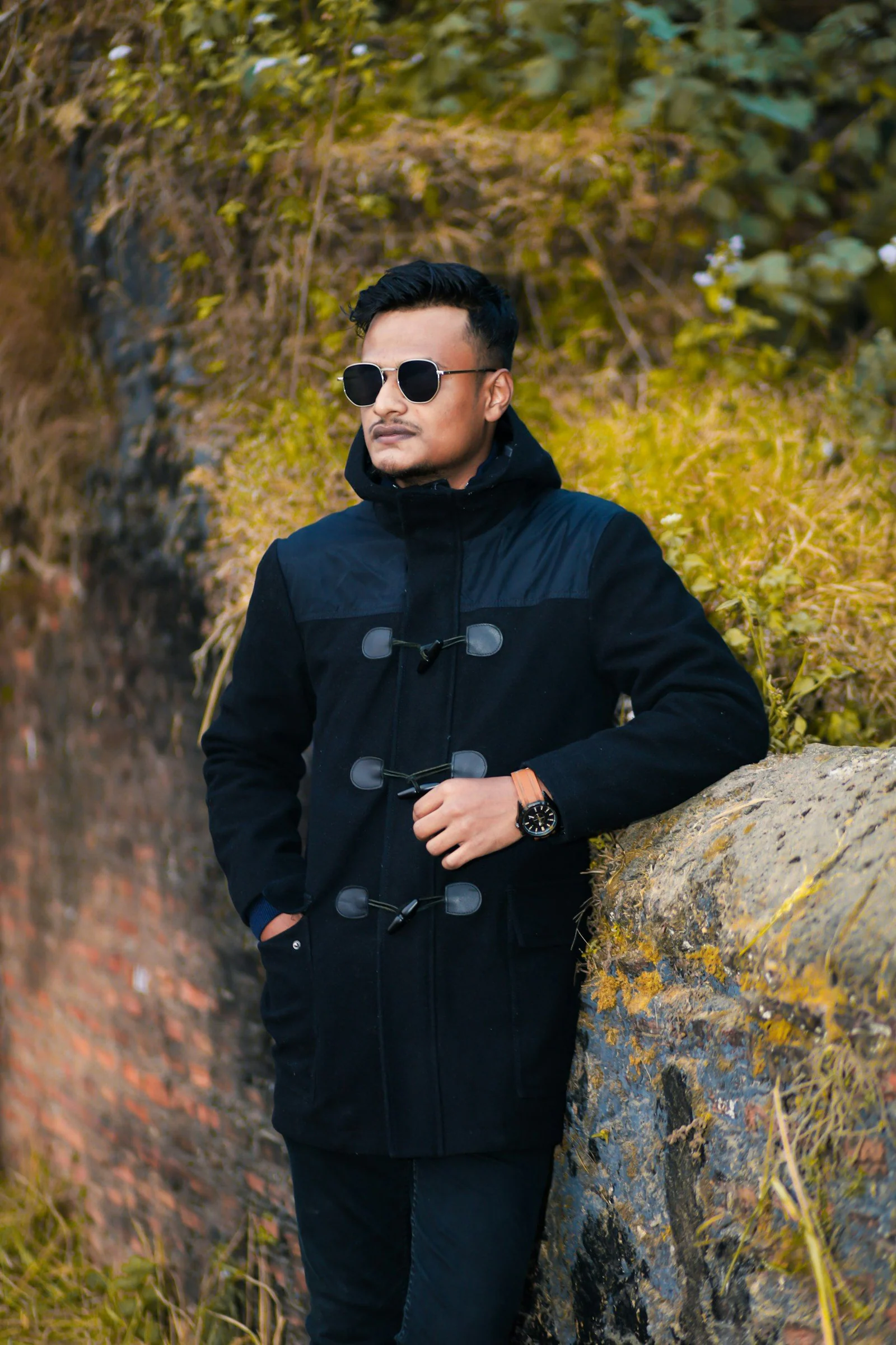 Man in duffle coat and sunglasses leaning on stone wall