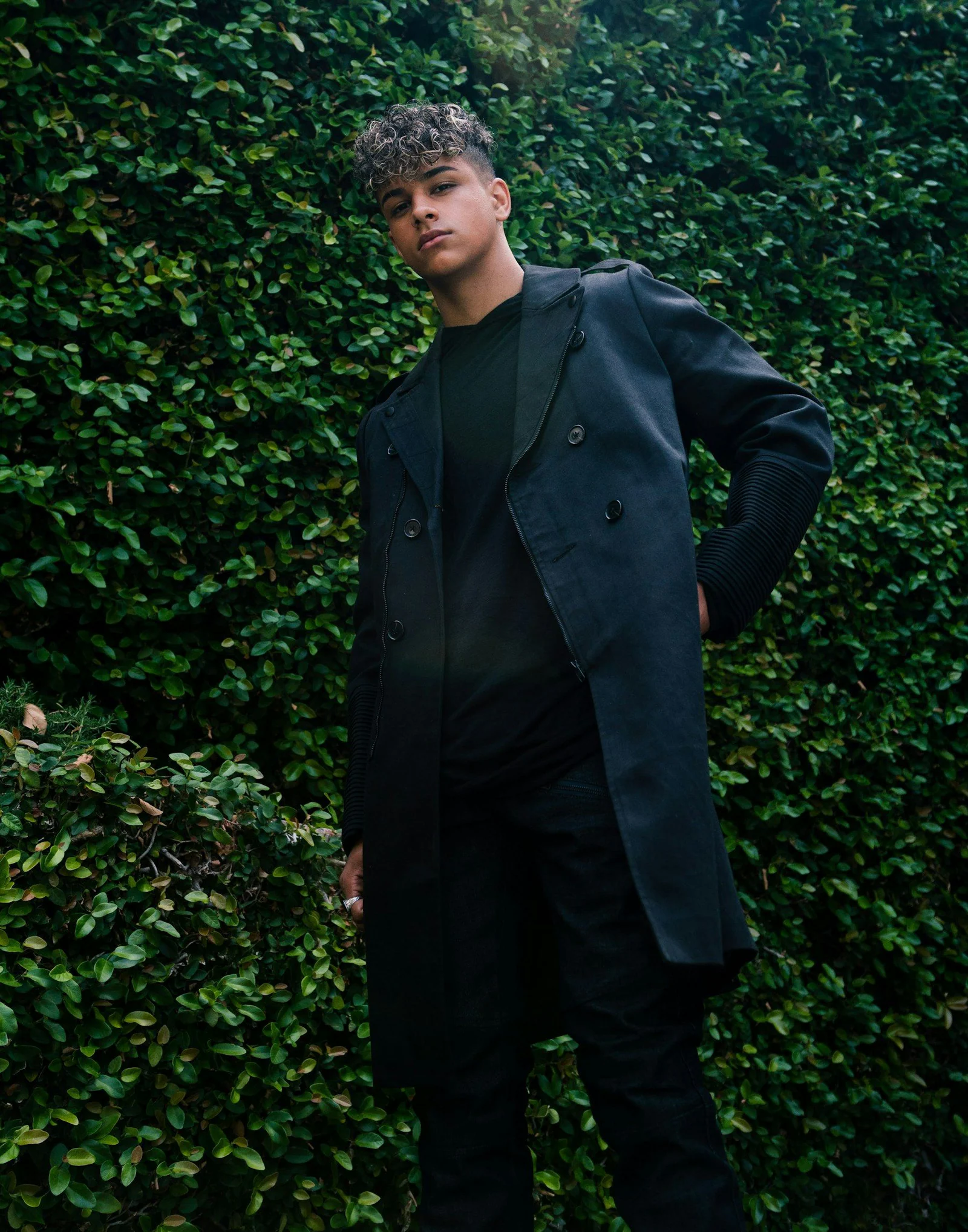 Man in black suit standing beside green plant