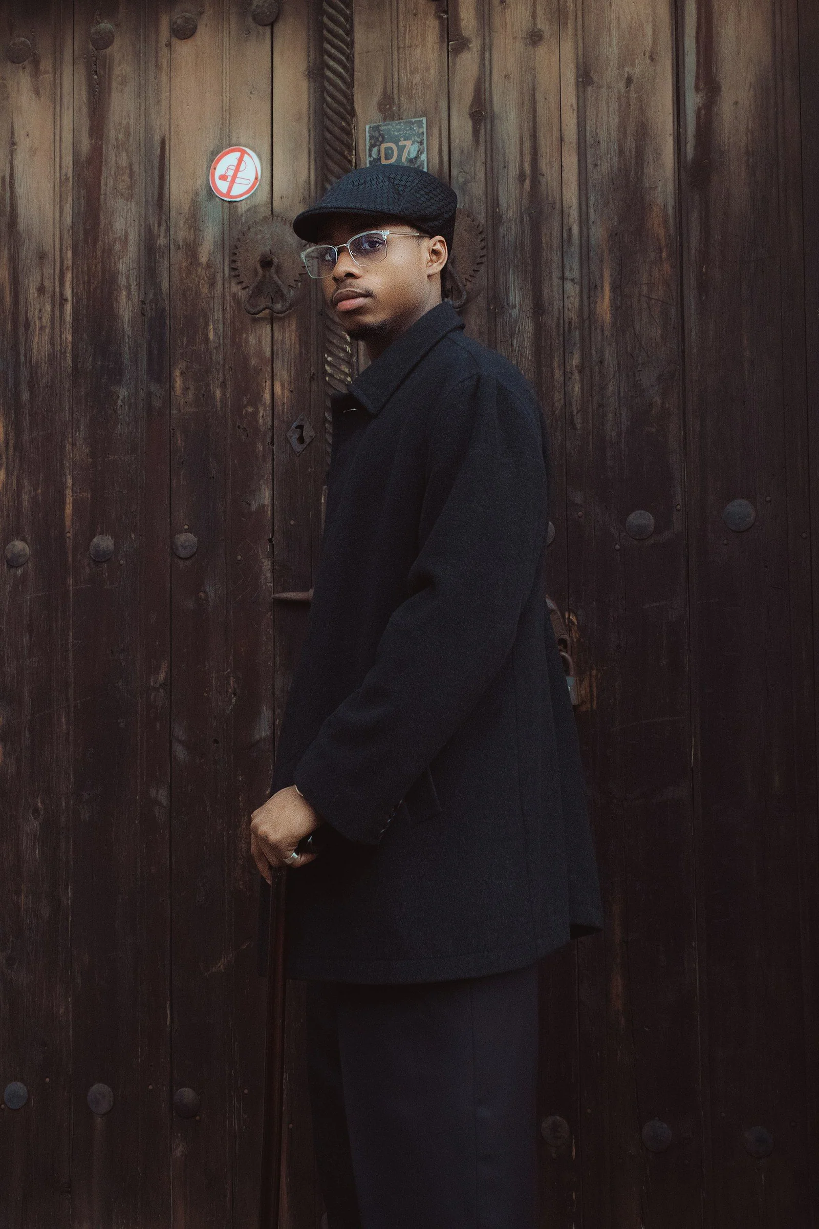 Man in black coat cap and glasses by wooden door
