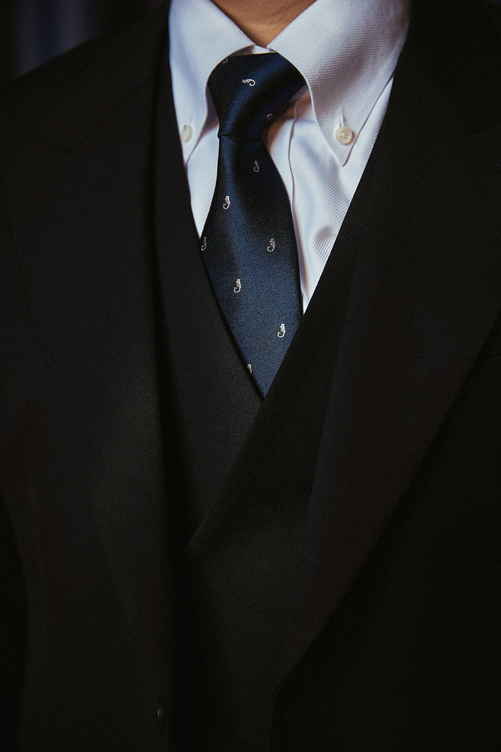 A black suit white shirt and patterned blue tie