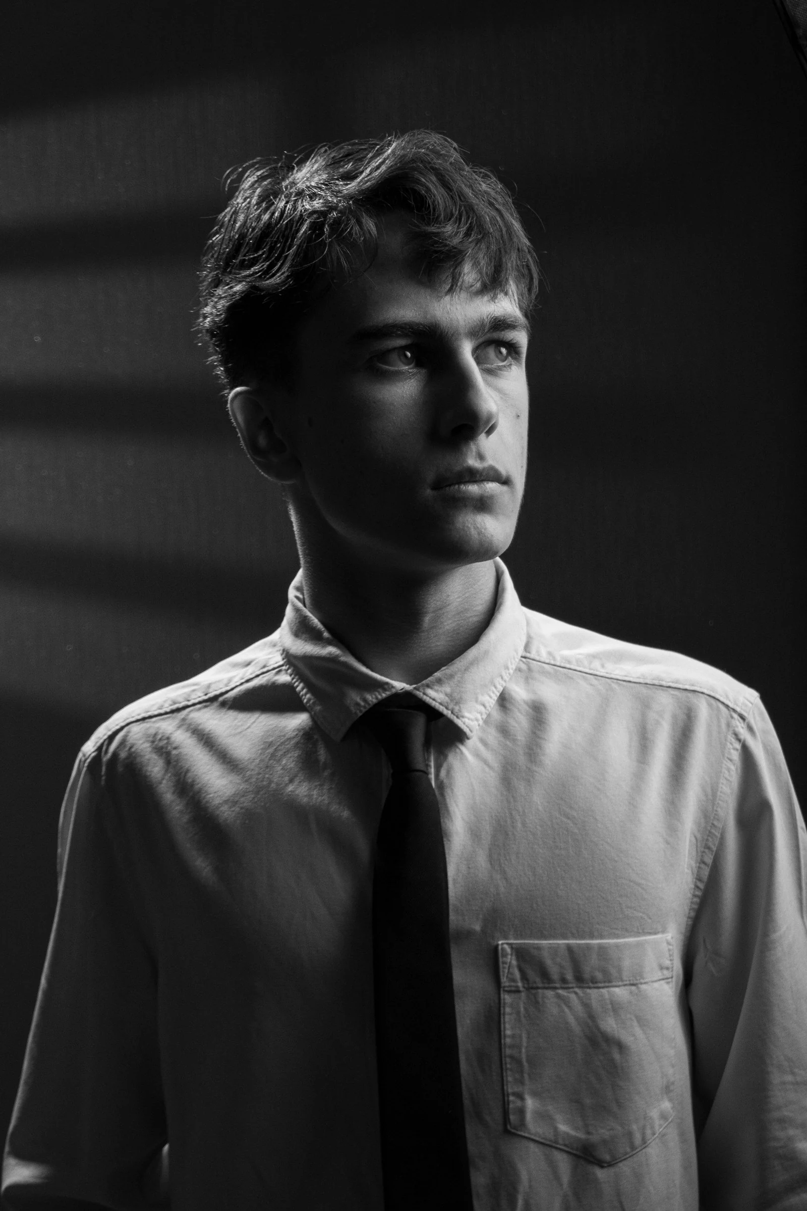 A young man in a shirt and tie looks away