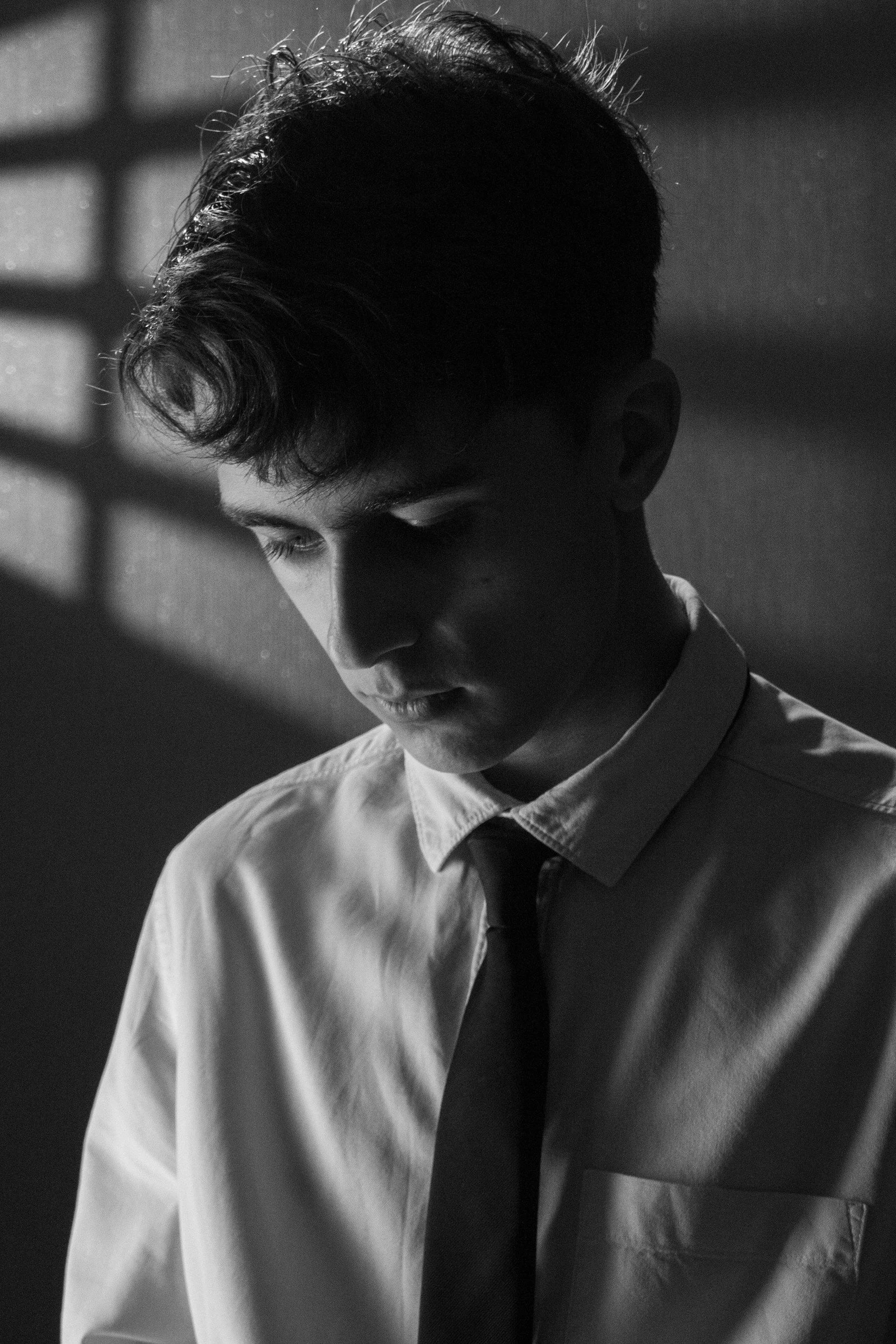 Young man in a collared shirt and tie looking down
