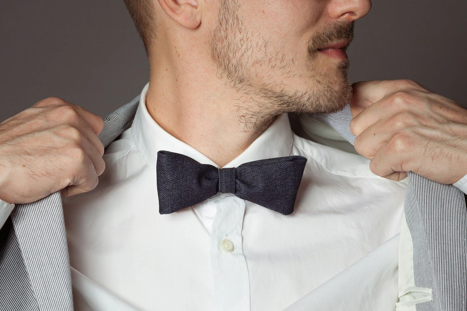 Man adjusting his grey suit jacket and dark bow tie