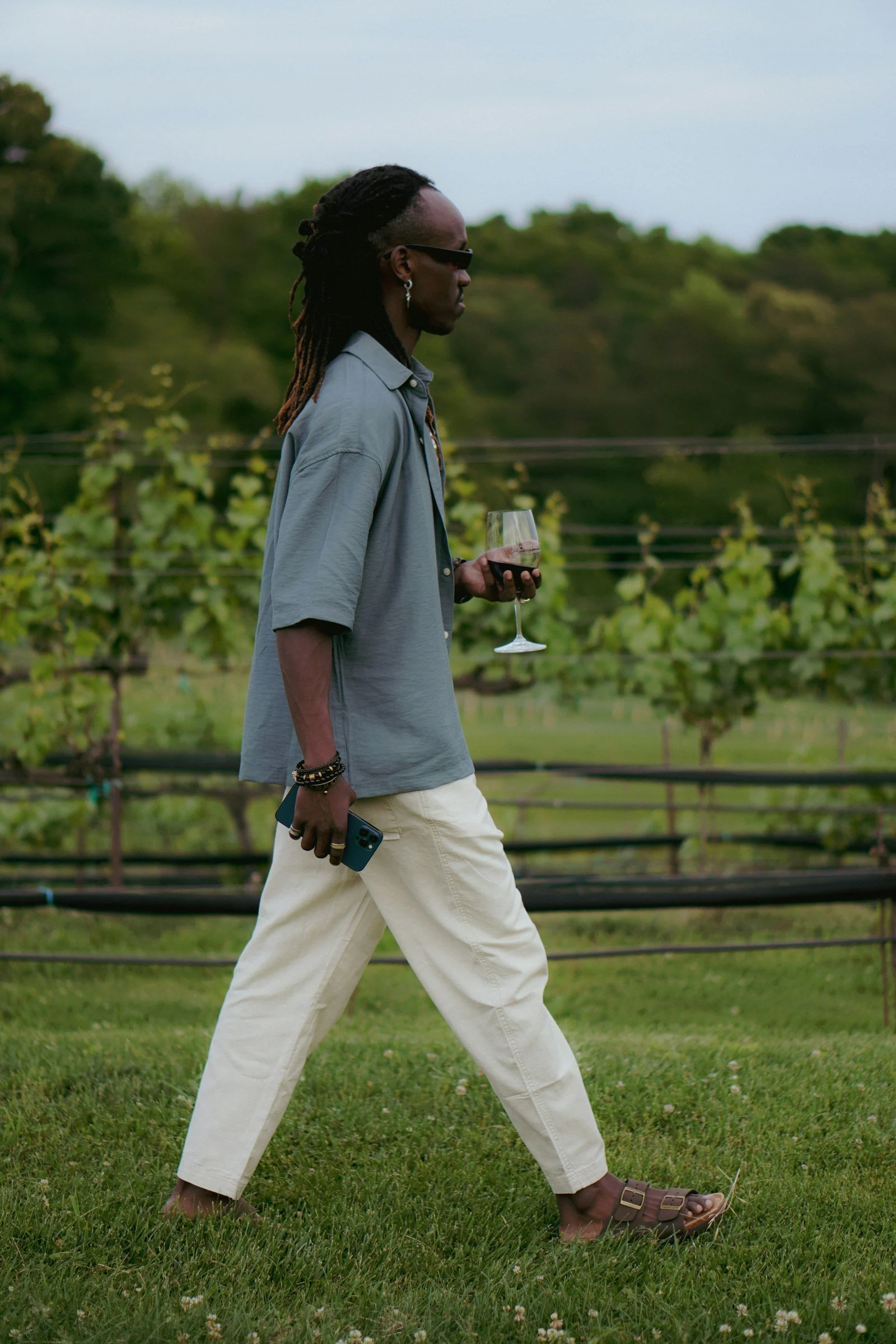 A man walking across a lush green field holding a glass of wine