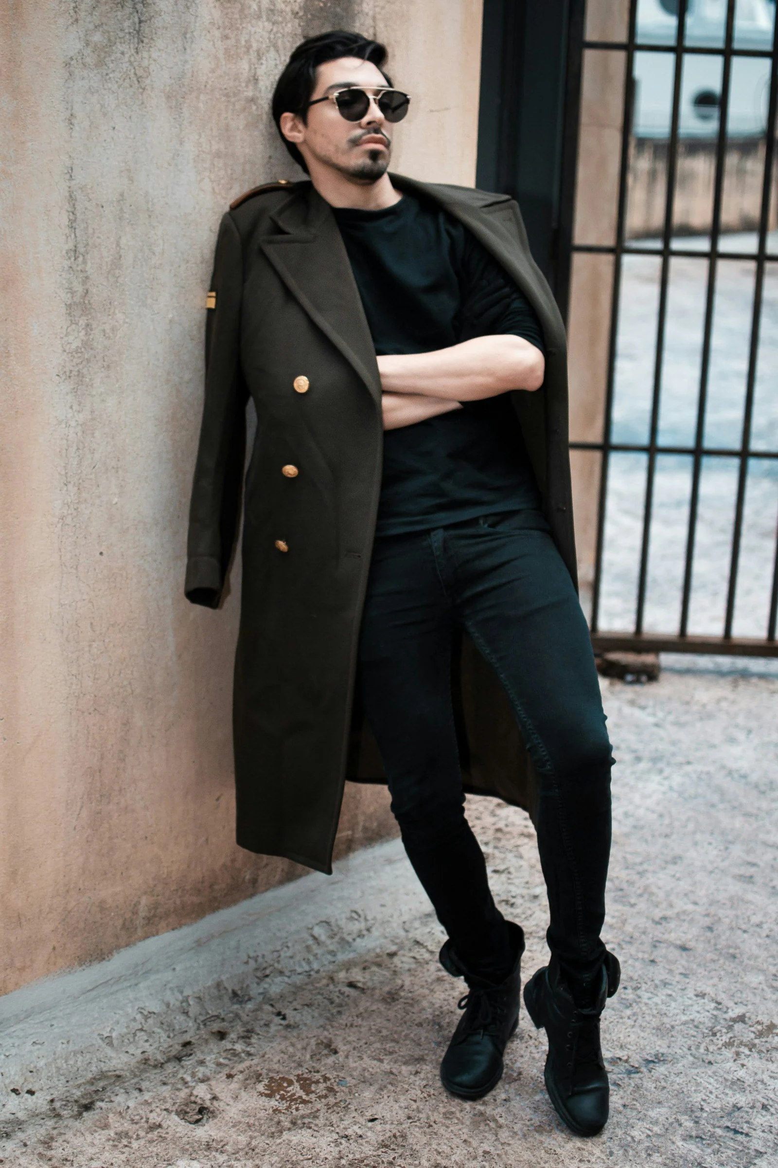 A man in a trench coat leaning against a wall
