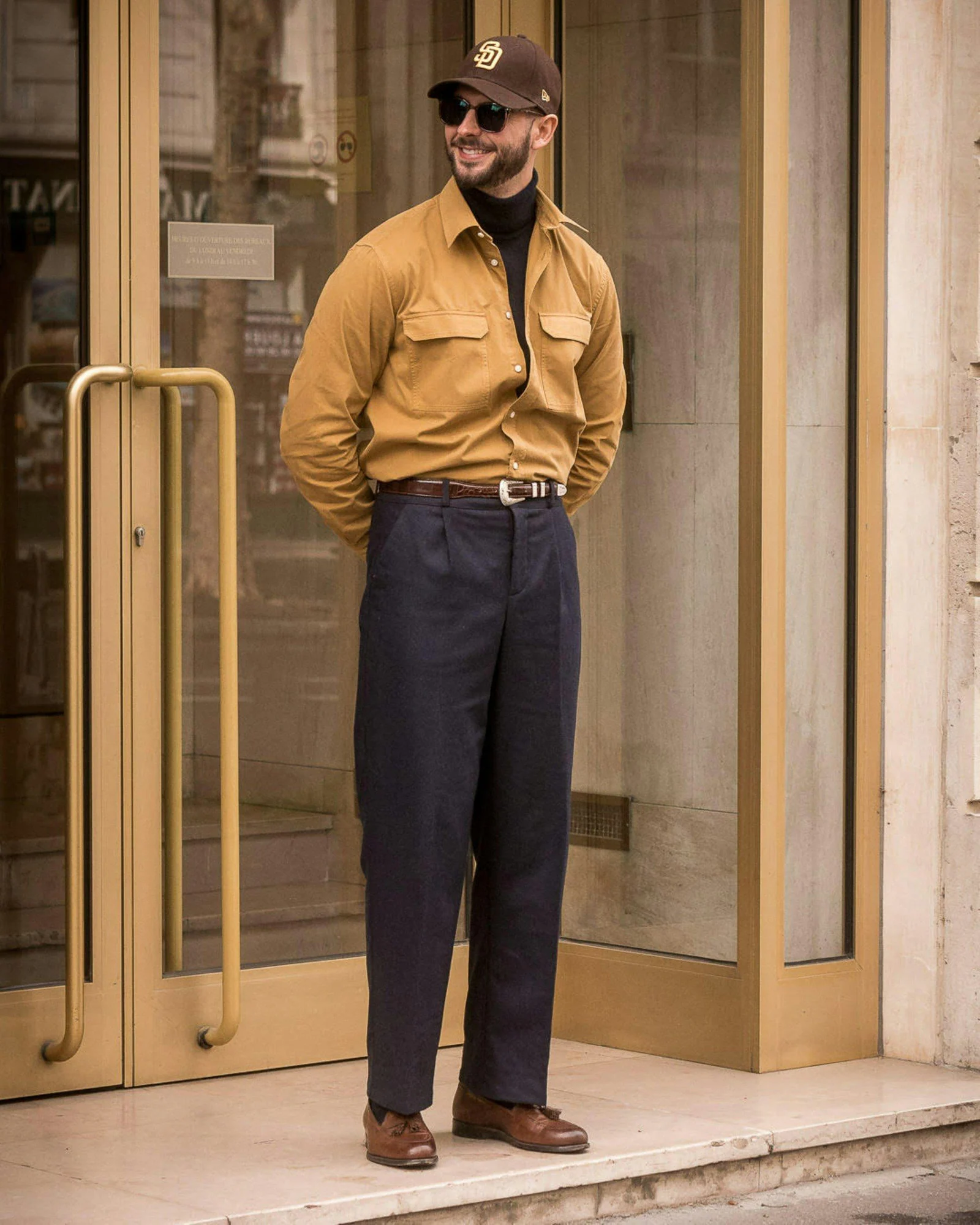 A man in stylish casual attire stands outside