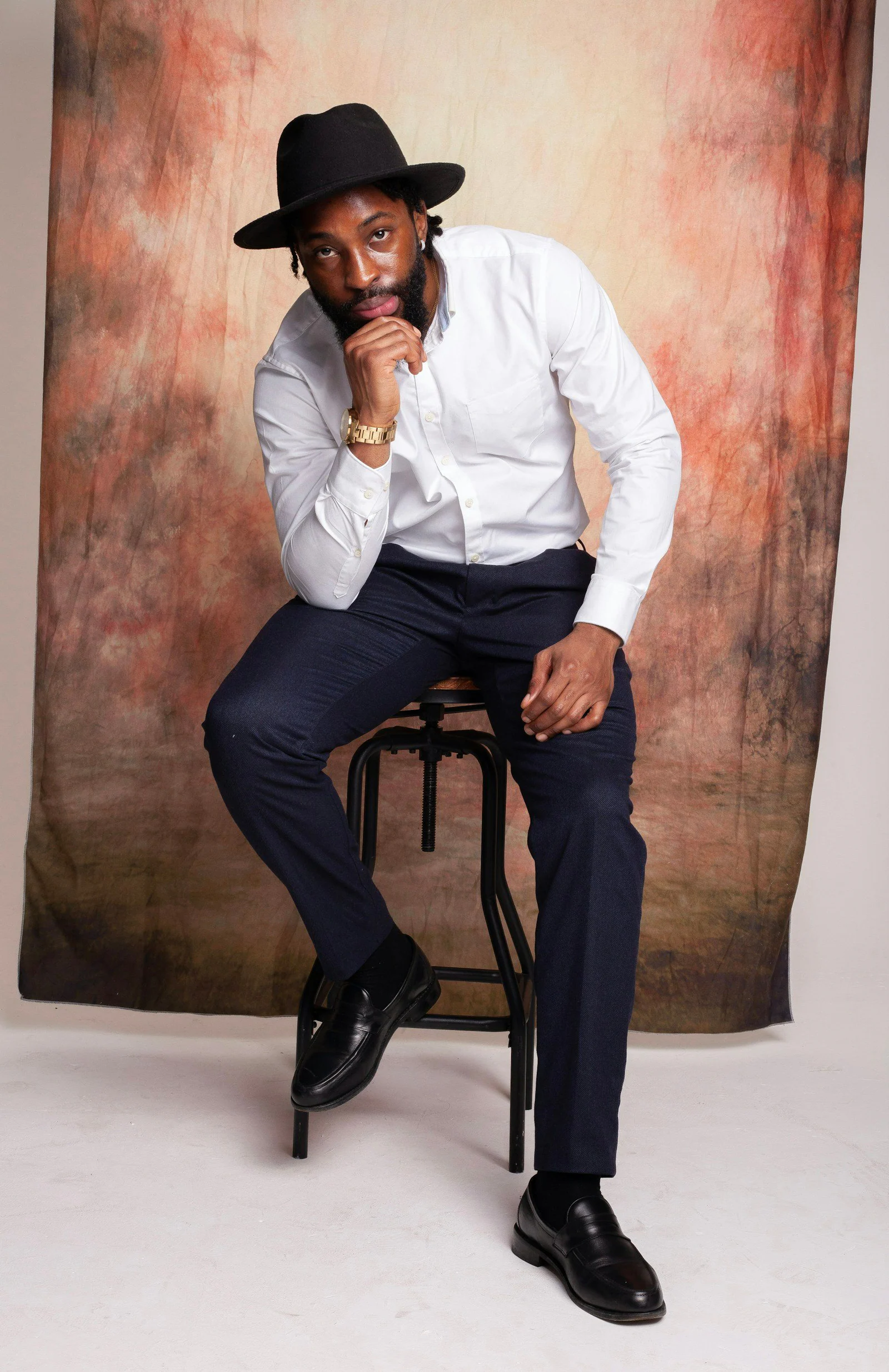 A man sitting on a stool wearing a hat