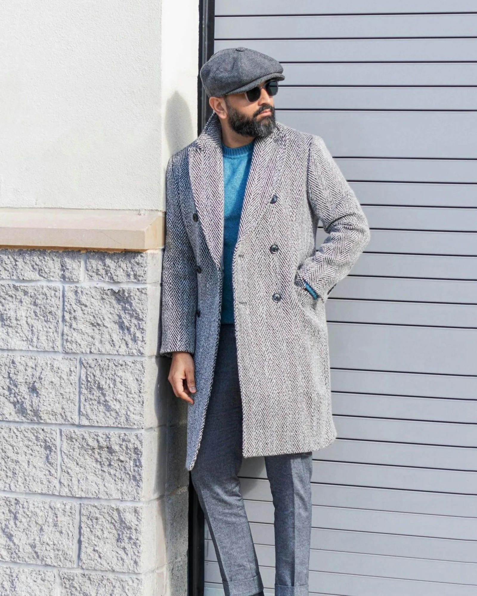 A man leaning against a wall wearing a coat and hat