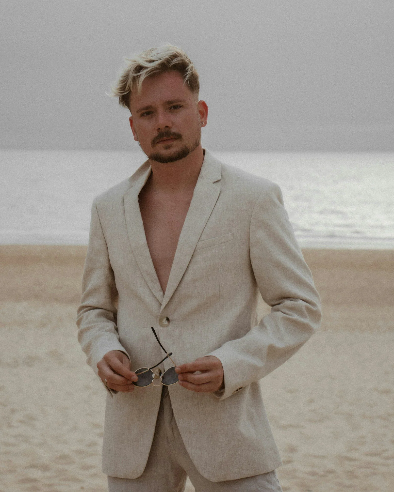A man standing on a beach holding a pair of scissors