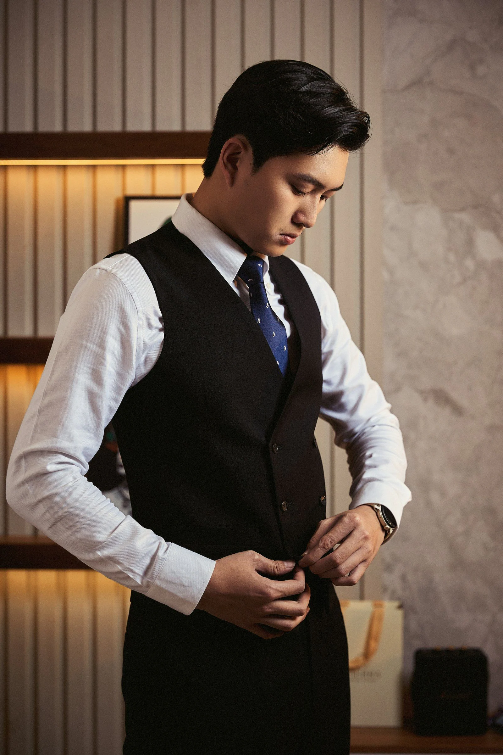 Stylish man buttoning his black vest indoors