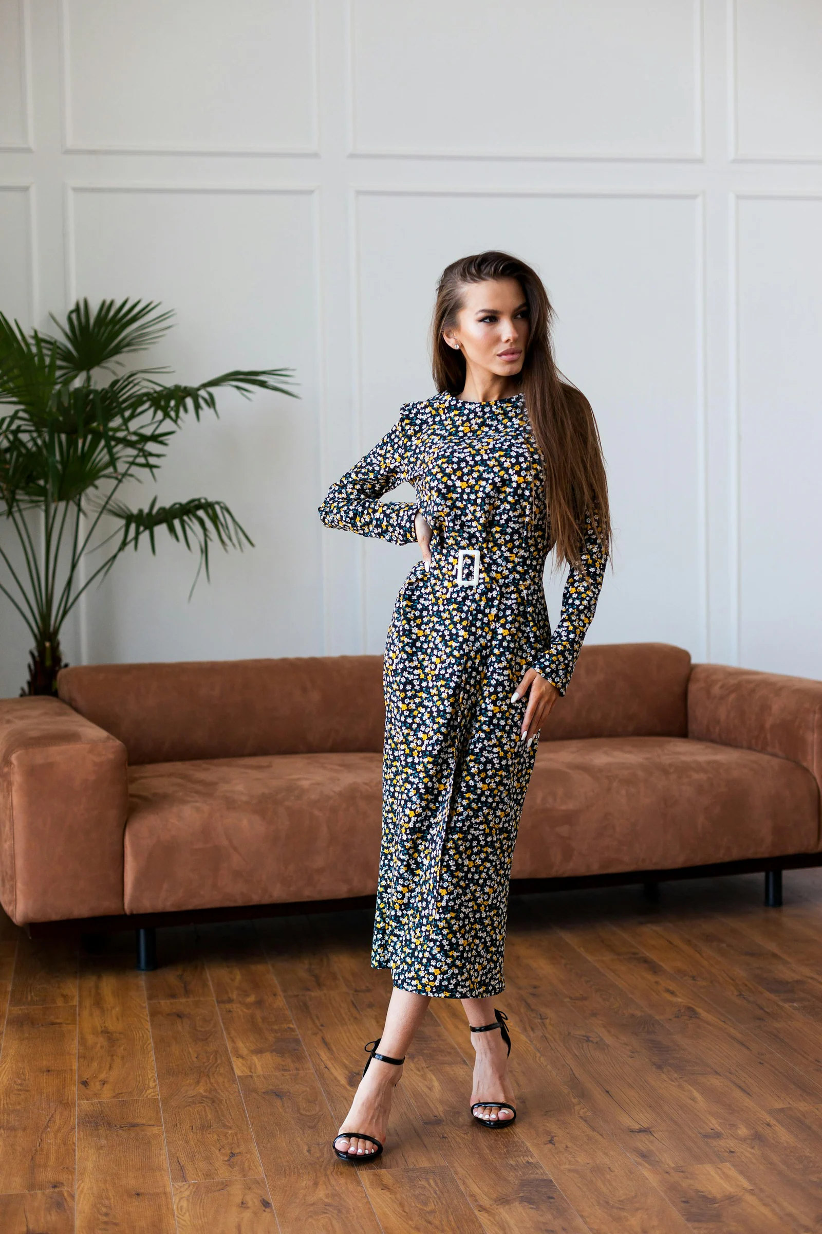 Woman in black and white floral long sleeve dress standing beside brown couch