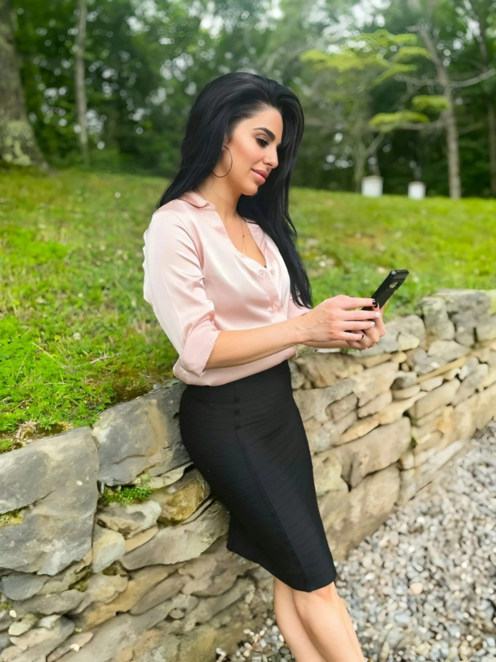 A woman leaning against a stone wall looking at her cell phone
