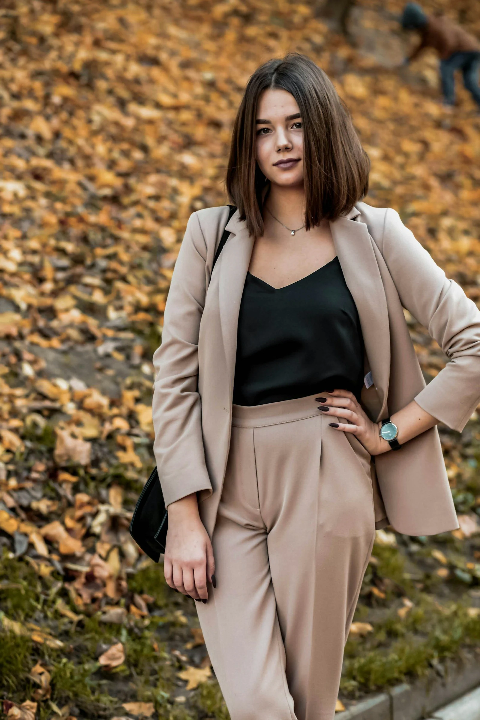 Woman in black tank top and beige blazer standing on dried leaves