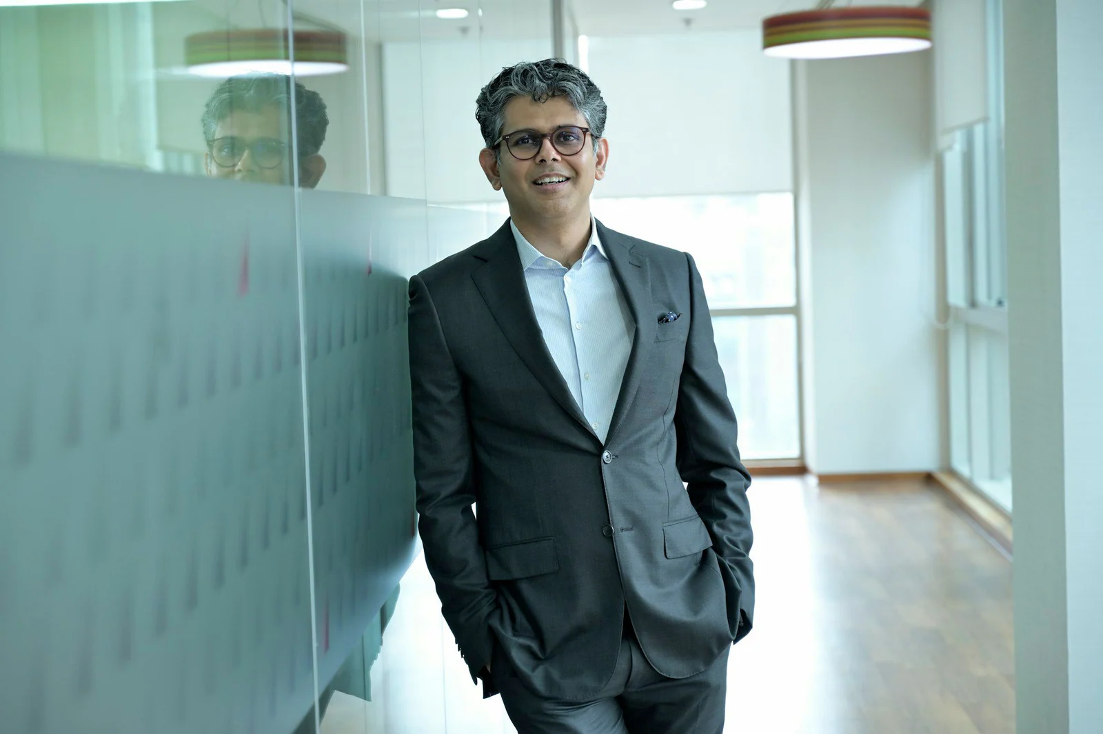 Man in a charcoal suit and open-collar shirt in an office corridor