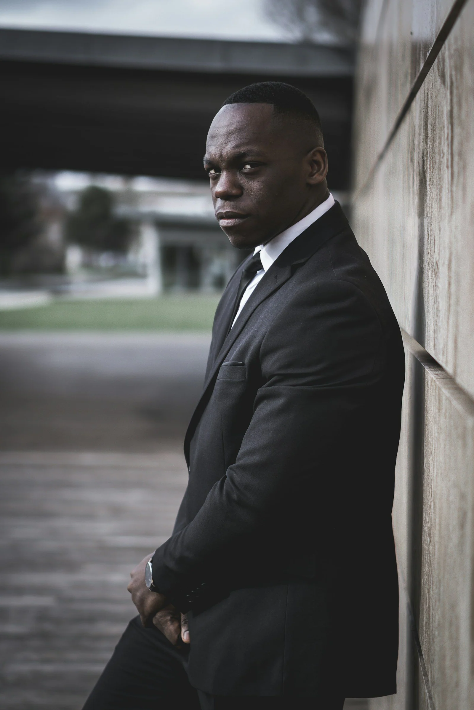 Black formal suit, man leaning against a wall