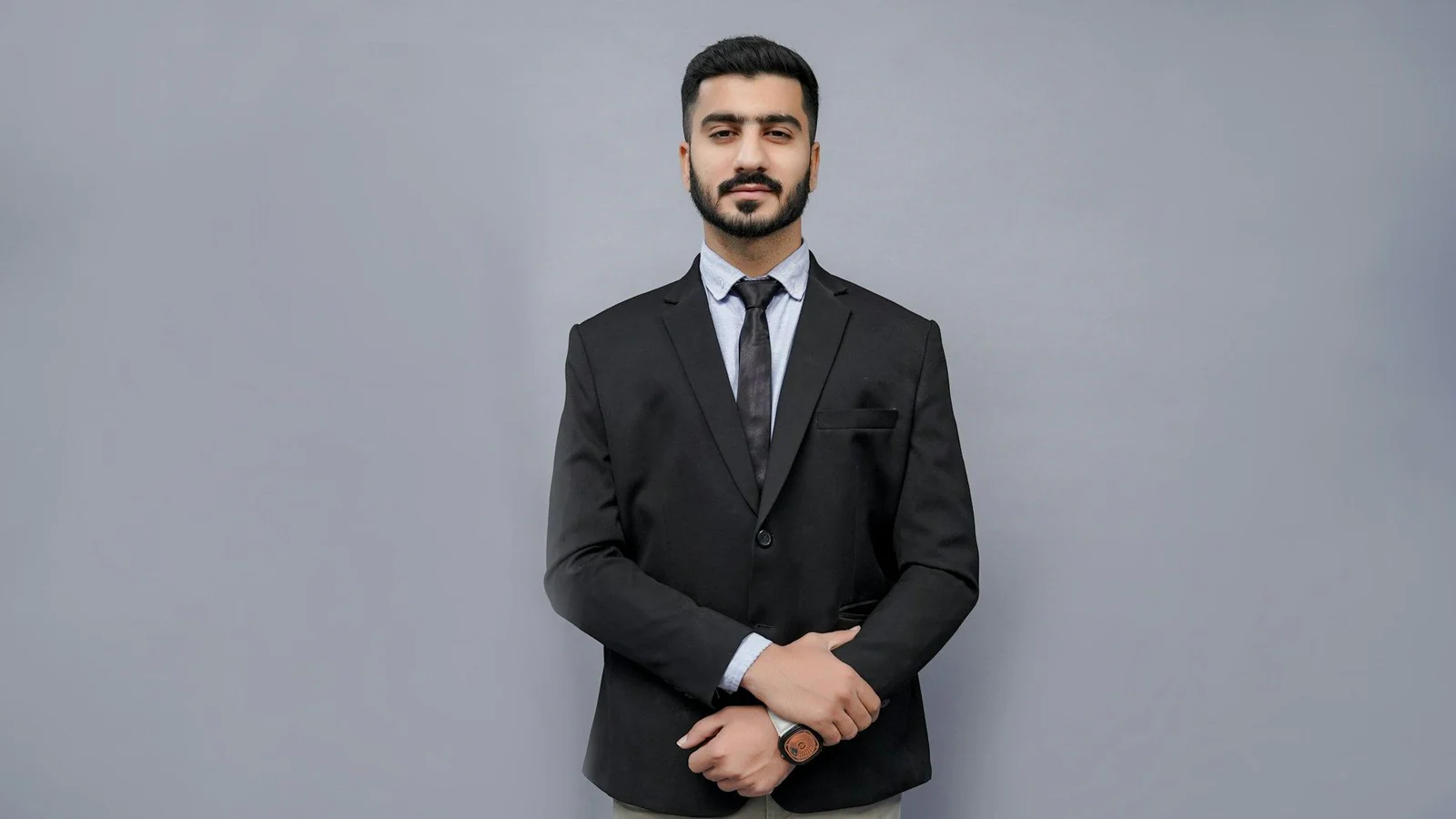 Man in a black two-piece suit and tie, studio portrait