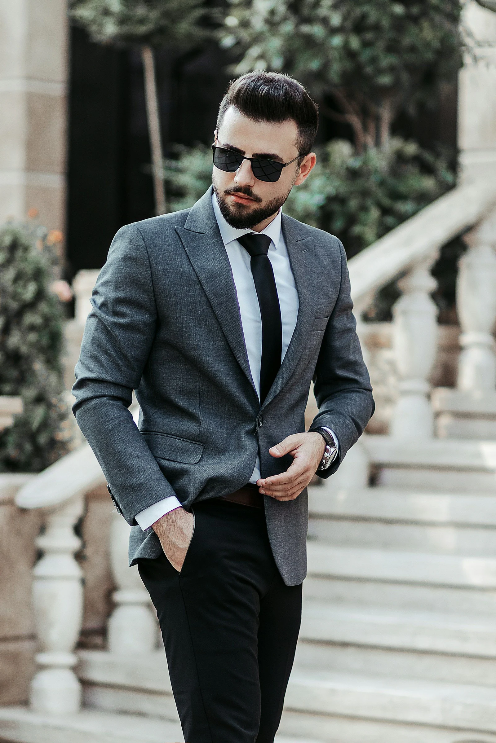 Grey two-piece suit with a black tie on stone steps