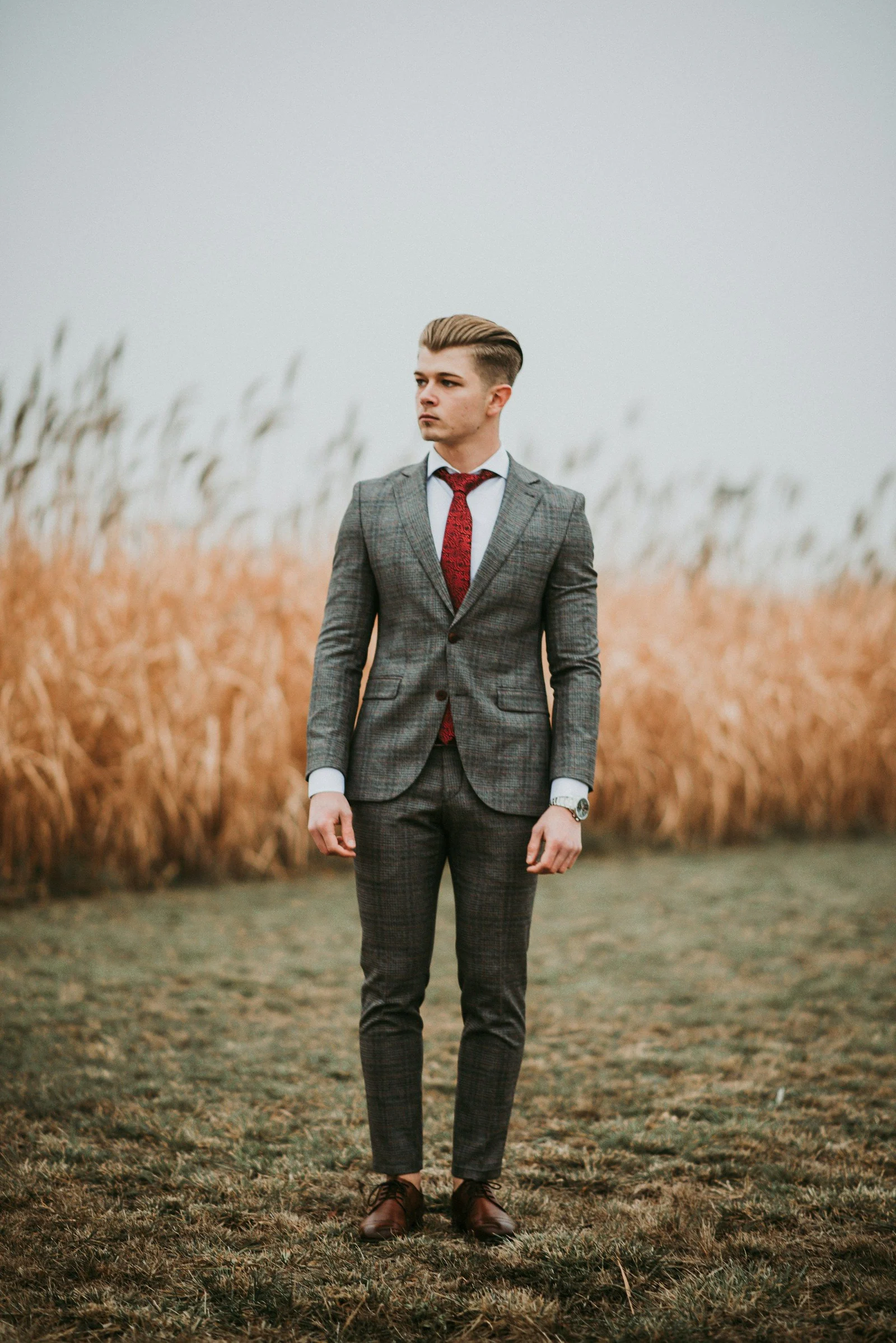 Groom in a grey suit and burgundy tie in a field of grass
