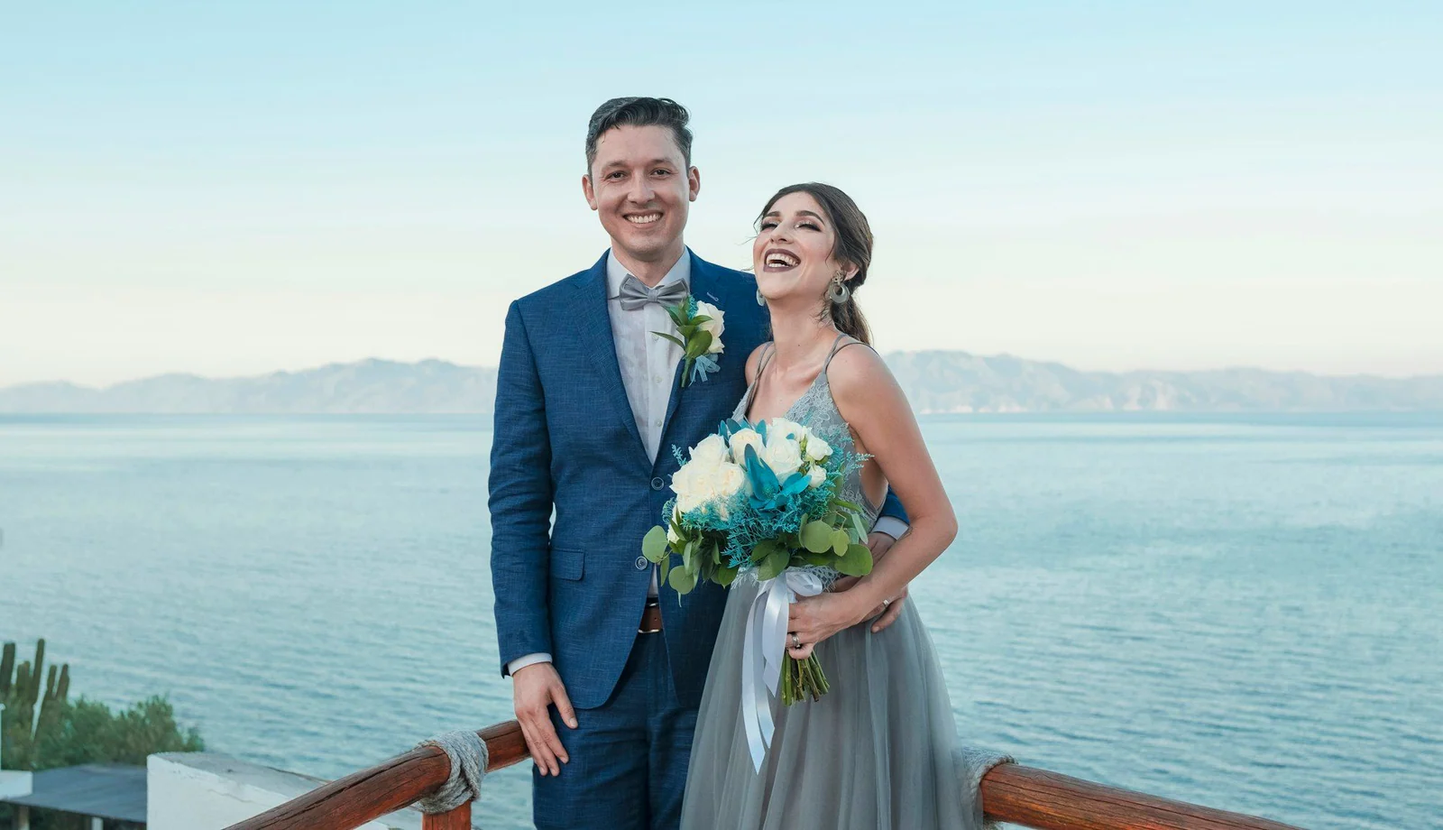 Groom in a navy suit with his bride by the sea